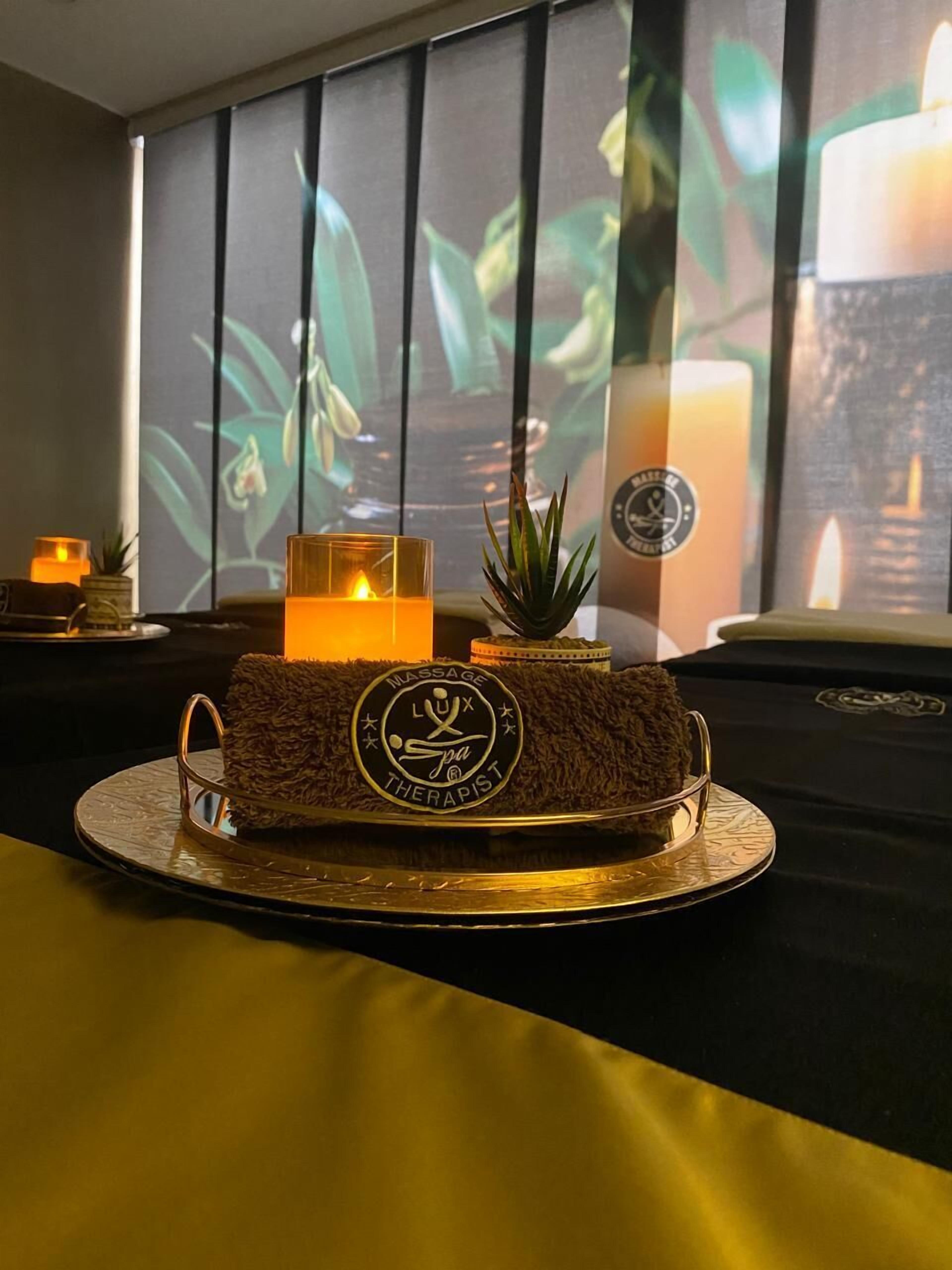 A massage therapist's logo on a plush cushion, a lit candle, and a small plant on a table with a window view in the background.