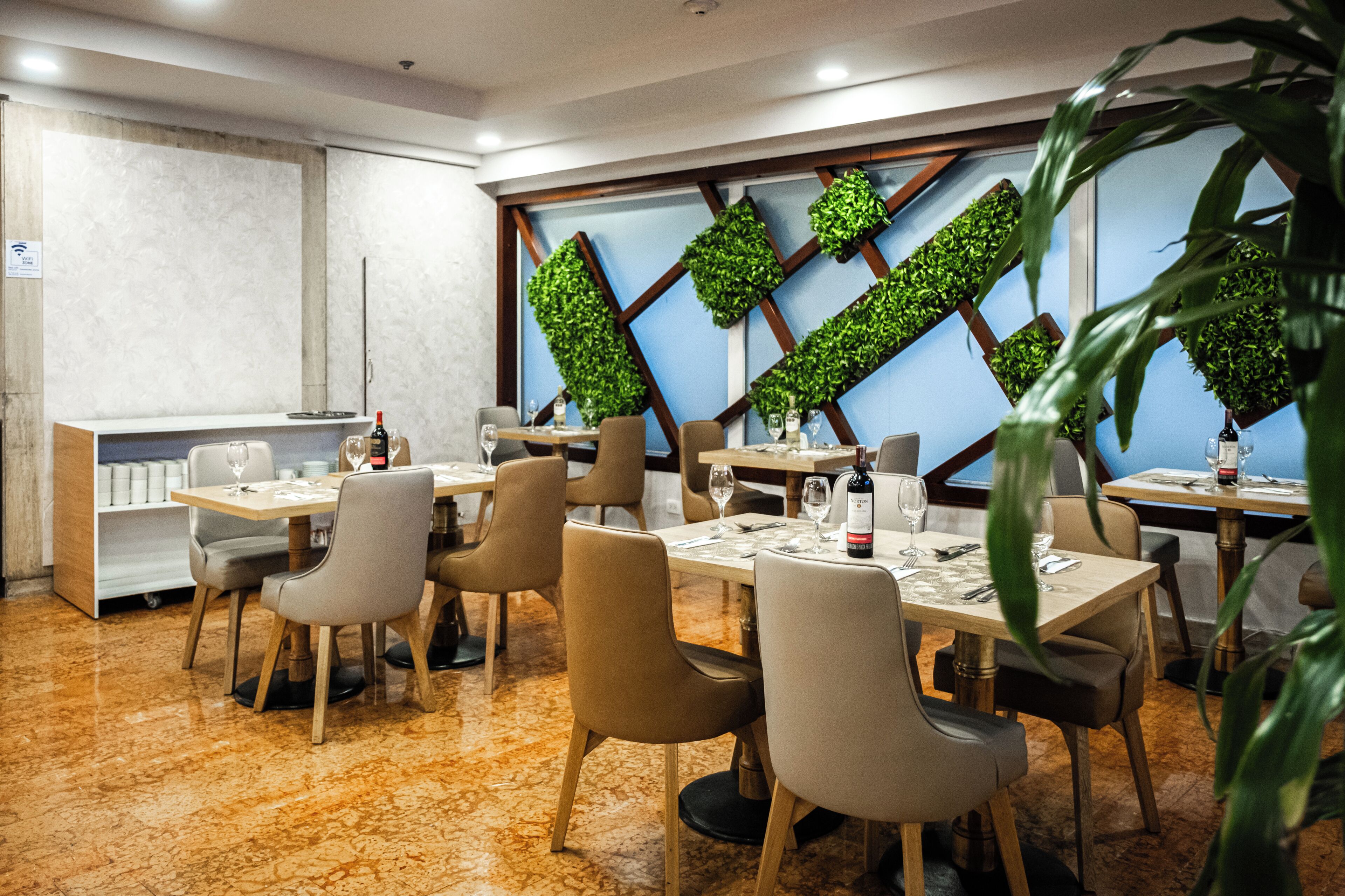 A modern dining area with rectangular tables, beige chairs, and a decorative green wall.