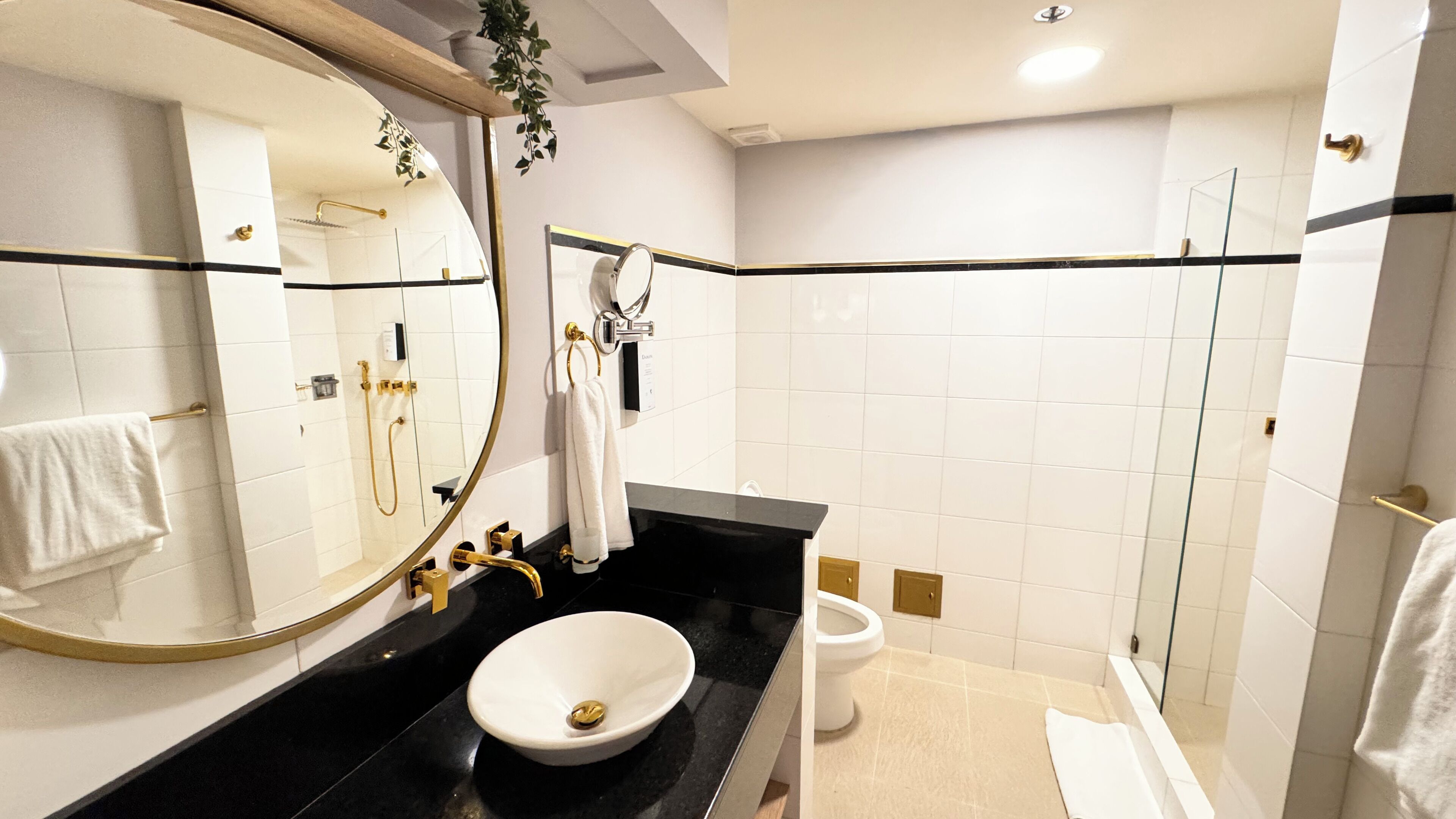 Un baño moderno con un espejo grande, encimera negra, lavabo blanco, inodoro y cabina de ducha de vidrio.