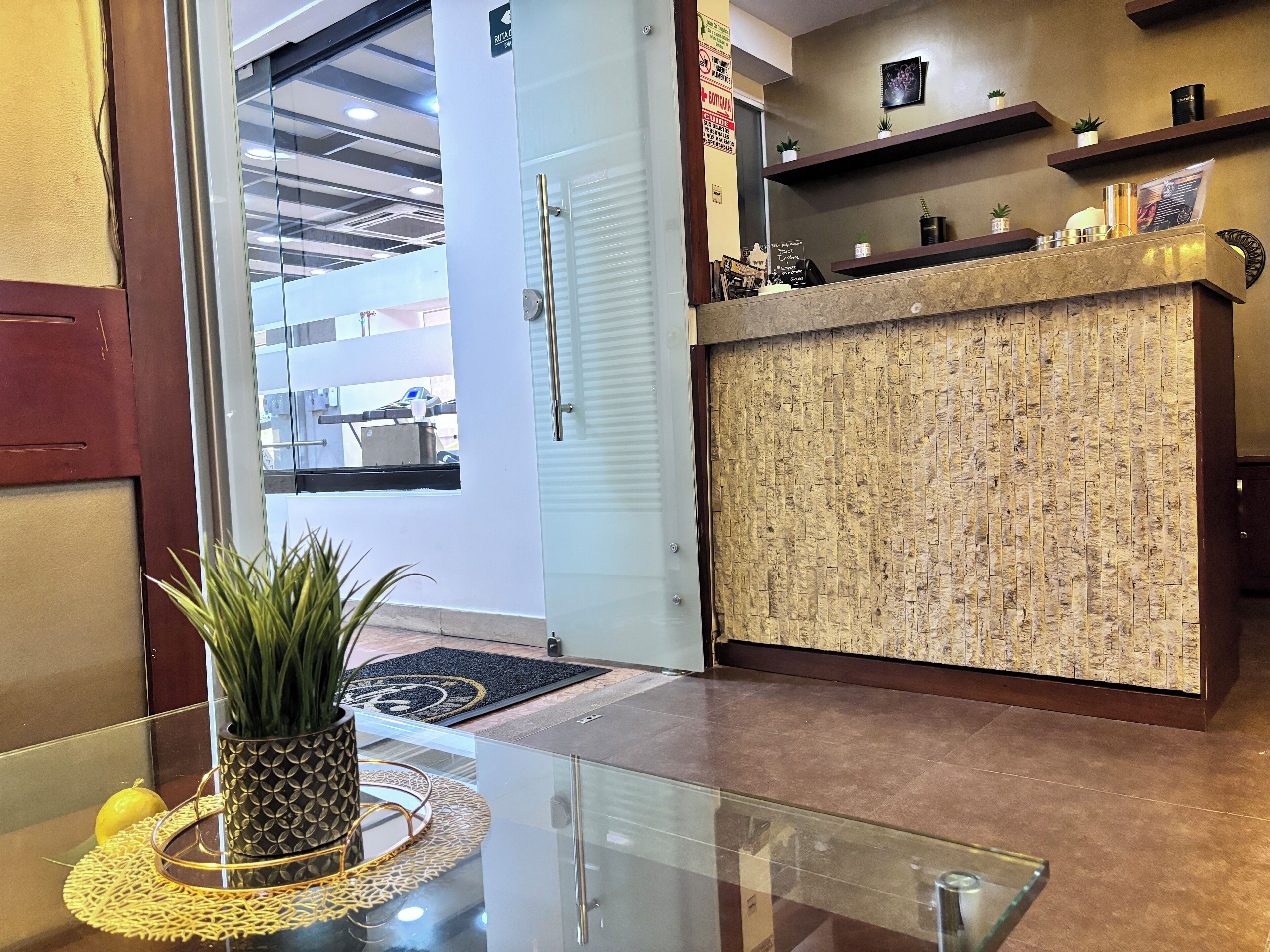 Uma área de recepção com balcão, planta em vaso e mesa de vidro.