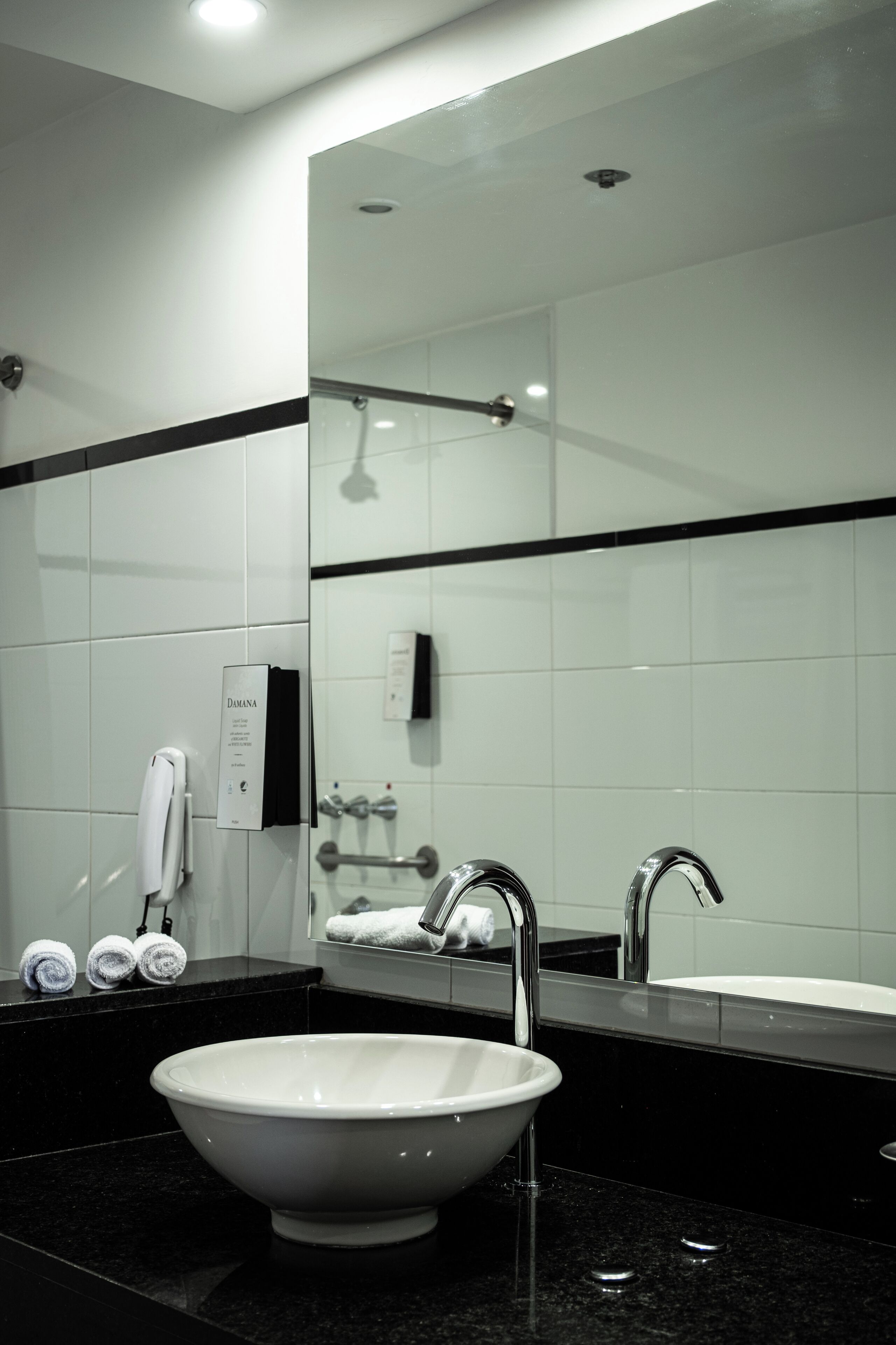 Een moderne badkamer met een grote spiegel, een witte wastafel, een zwart aanrecht en een handdouche.