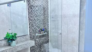 Un baño moderno con ducha de vidrio, inodoro, lavamanos con planta y salpicadero de azulejos.
