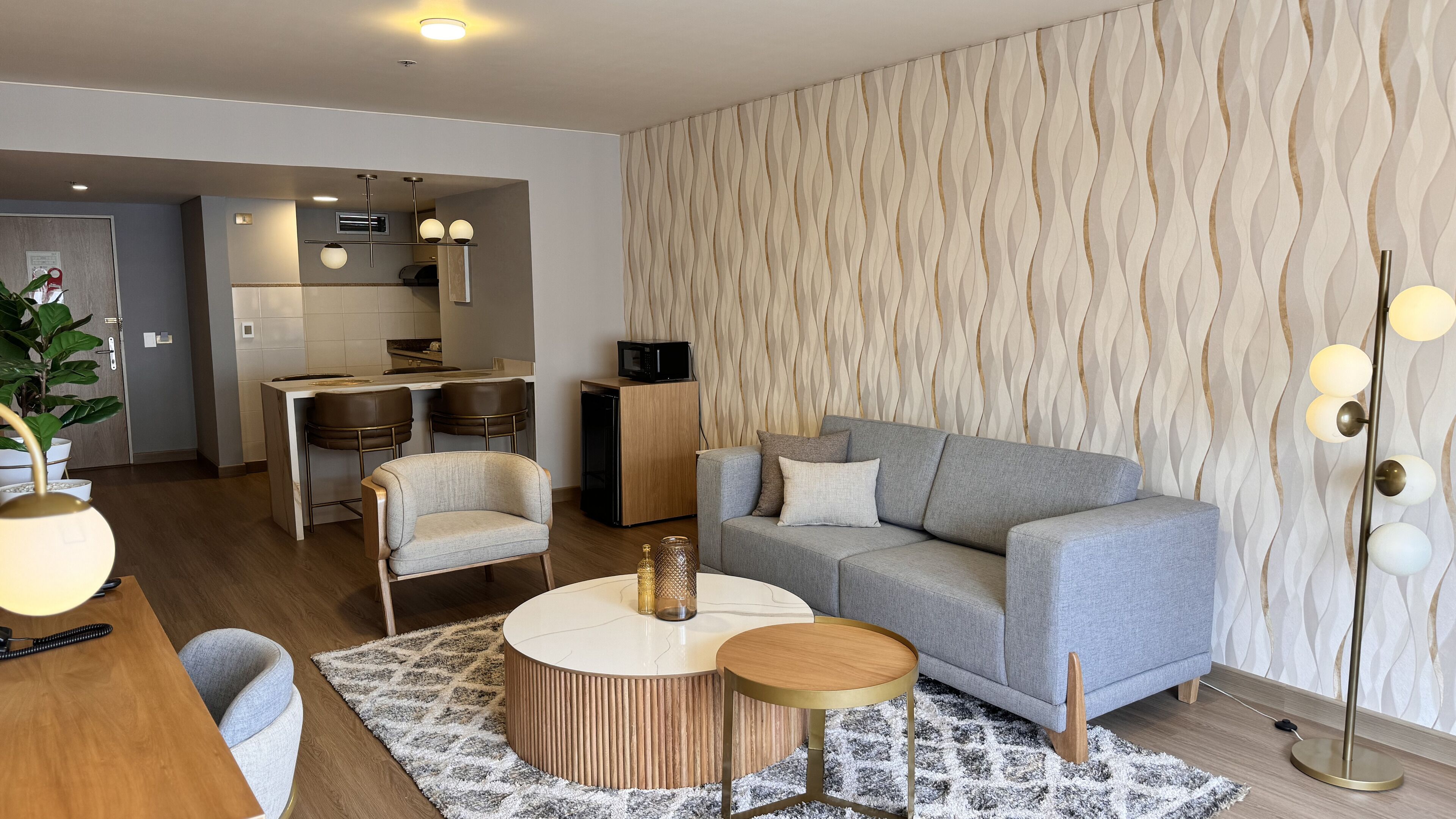 Een moderne woonkamer met een grijze bank, twee fauteuils, een salontafel en een keuken op de achtergrond.