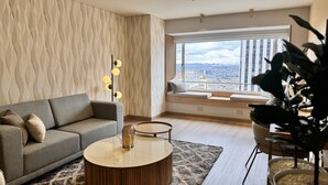 A modern living room with a grey sofa, a round coffee table, and a view of the city through large windows. -  Tequendama Suites Bogota (Bogotá)