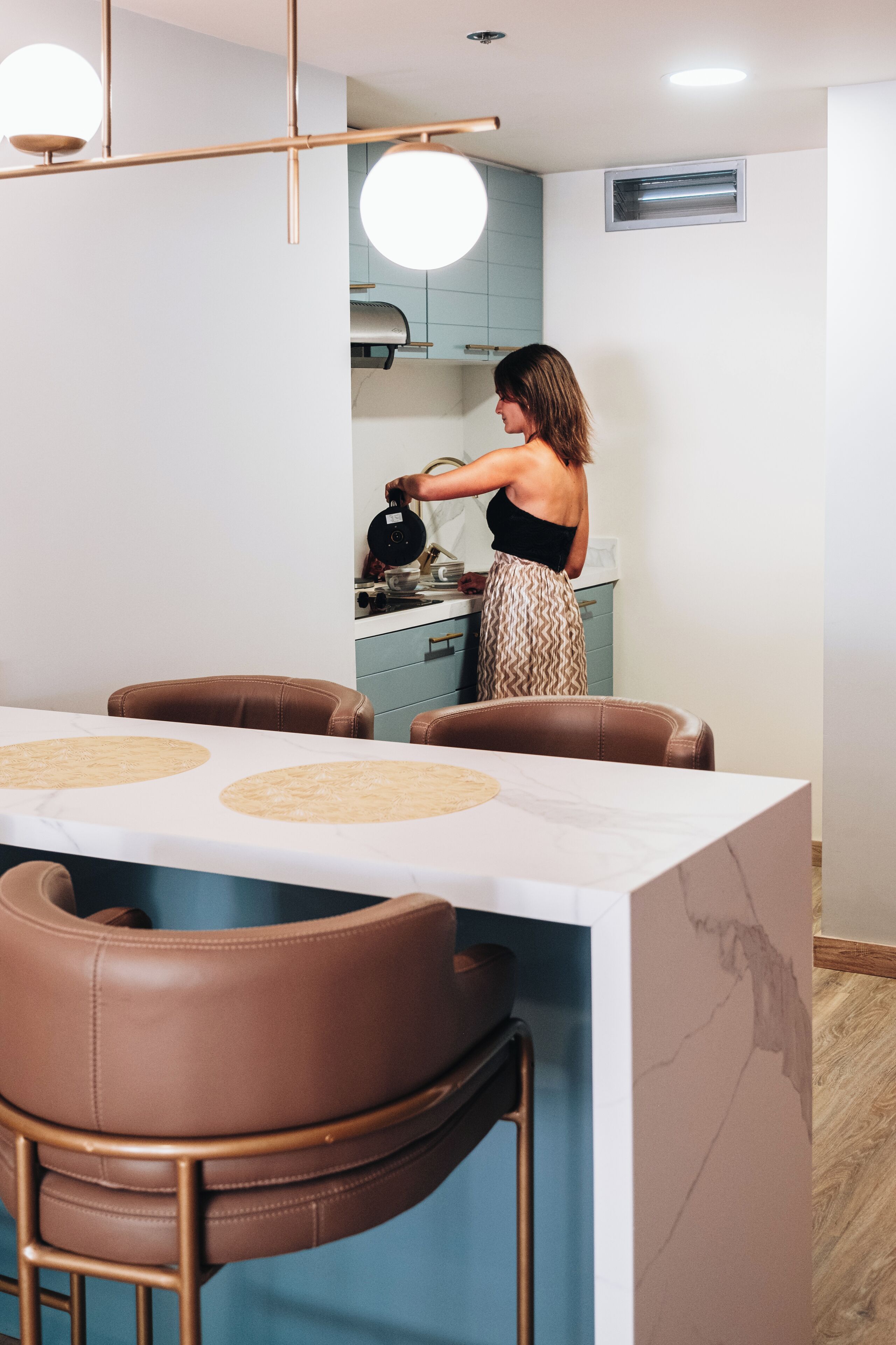 A modern kitchen with a person cooking, a dining area with leather chairs, and a marble countertop.
