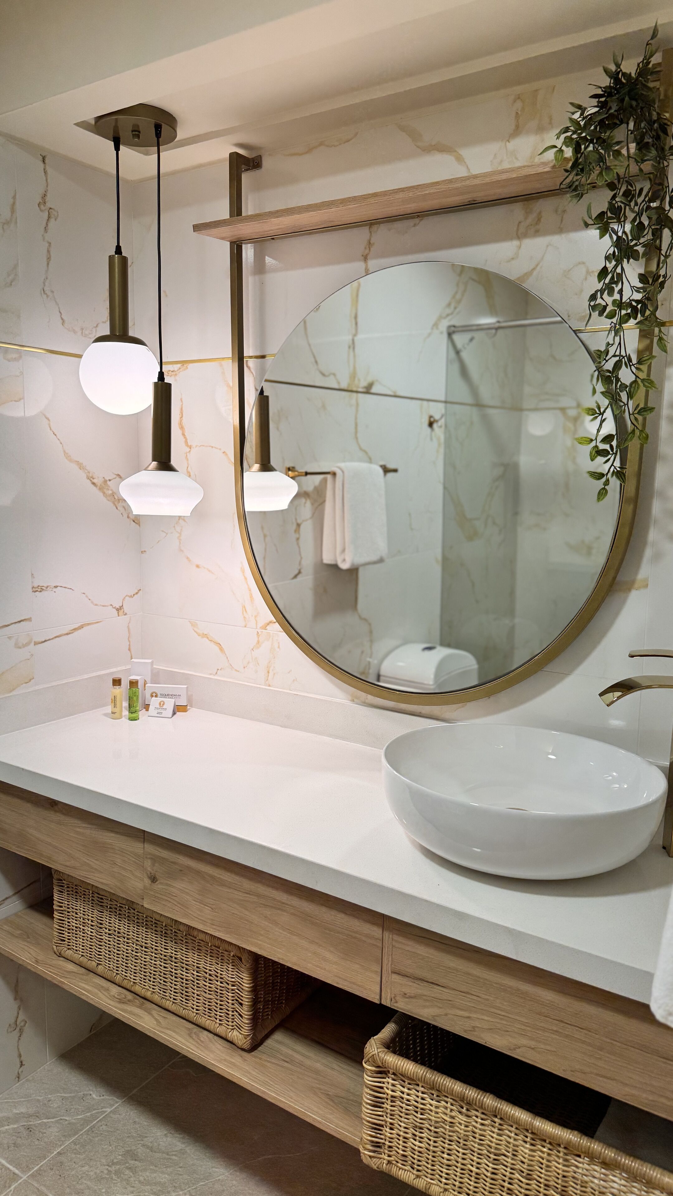 Un bagno con parete in marmo, uno specchio rotondo, un lavandino bianco e due lampade a sospensione.