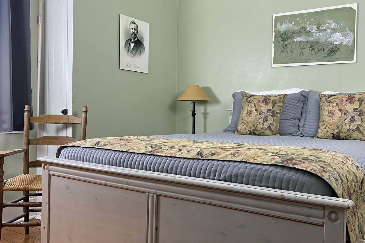 A bedroom with a bed, a chair, a lamp, and two framed pictures on the wall.