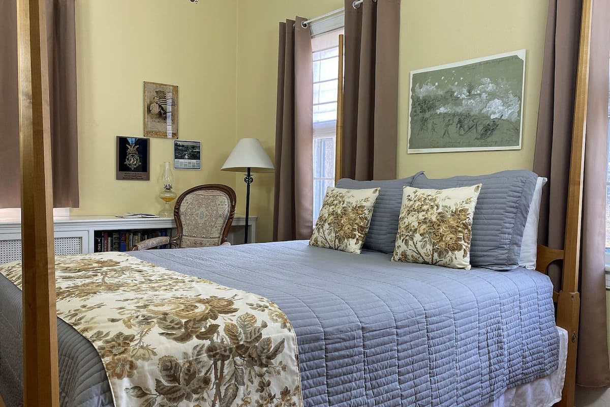 A neatly arranged bedroom with a large bed, a chair, a desk, and a lamp.