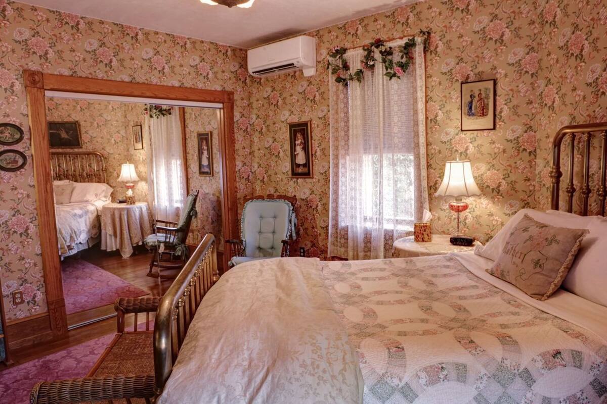 Une chambre à coucher avec un grand lit, une chaise, une petite table et un miroir.