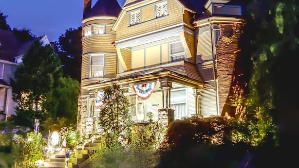 Una casa grande e histórica con múltiples chimeneas, una entrada principal destacada y un jardín bien cuidado.