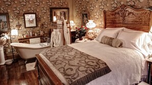 Un dormitorio clásico con una cama grande, una bañera antigua y un papel tapiz floral.