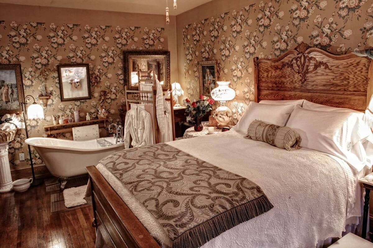 Une chambre à coucher classique avec un grand lit, une baignoire ancienne et un papier peint à motifs floraux.