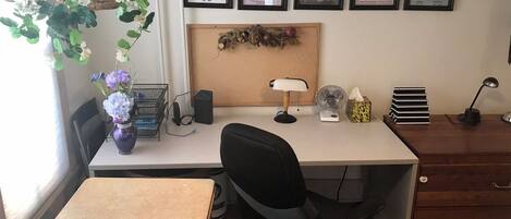 Un despacho en casa con un escritorio, una silla y diversos útiles de oficina. Hay cuadros en la pared y una planta en el escritorio.