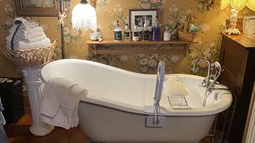 A classic clawfoot bathtub with a wooden vanity and a shelf with toiletries.