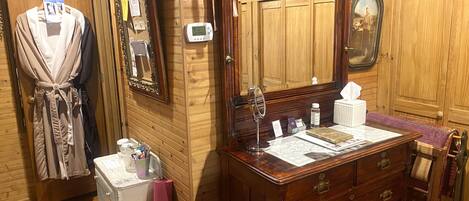 A wooden-paneled room with a vanity, a mirror, a robe, and a small table with toiletries.
