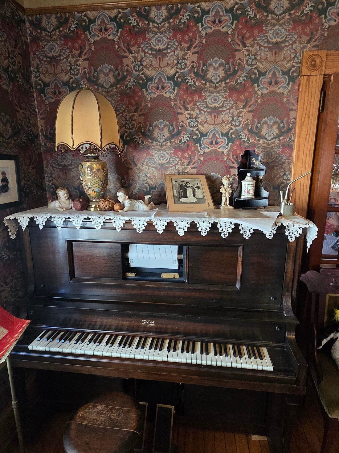 A piano with a lace tablecloth, a lamp, and decorative items on top.