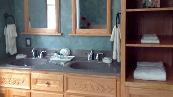 A bathroom with two sinks, wooden cabinets, and a shelf with folded towels.