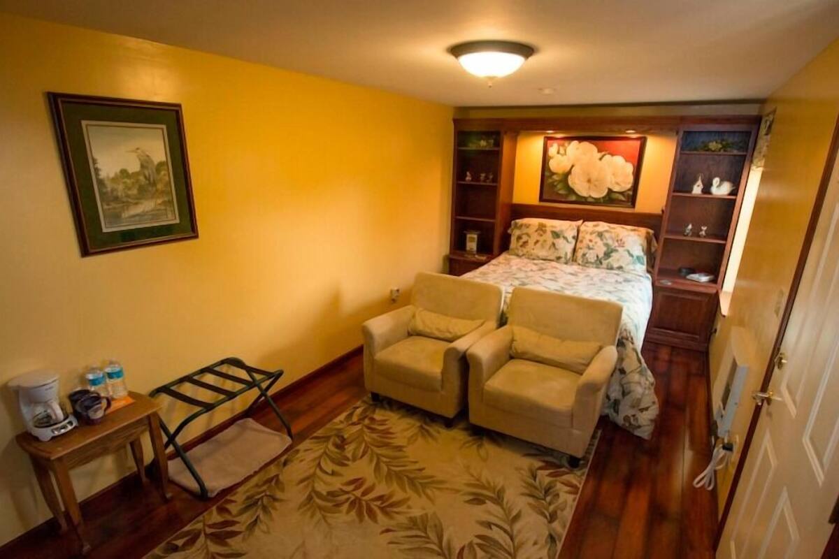 Quarto com cama, duas poltronas, mesa de centro e mesa de cabeceira.