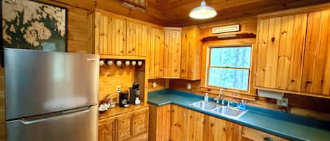 A wooden cabin kitchen with a refrigerator, wooden cabinets, a sink, and a window.