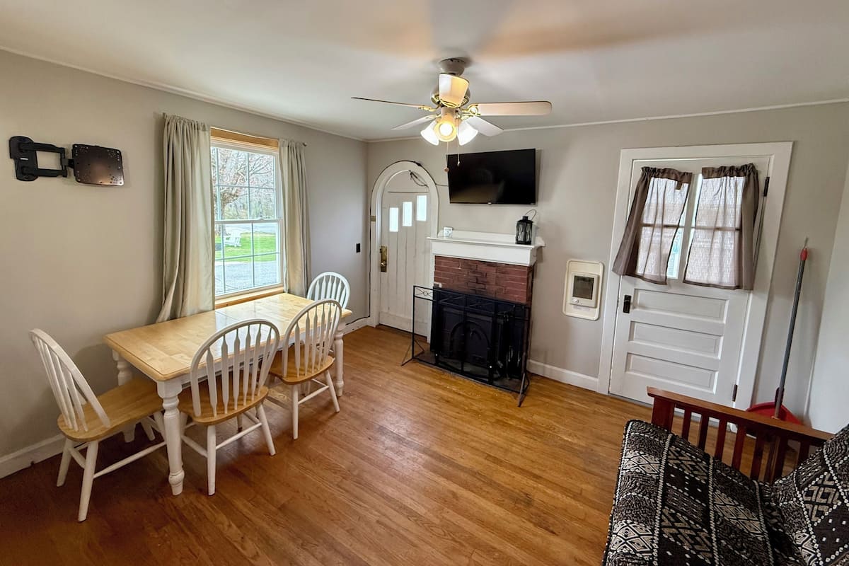 A dining area with a wooden table and chairs, a fireplace, a ceiling fan, and a TV mounted on the wall.