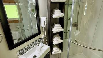 A modern bathroom with a glass shower enclosure, a vanity with a mirror and sink, and a towel rack with neatly folded towels.