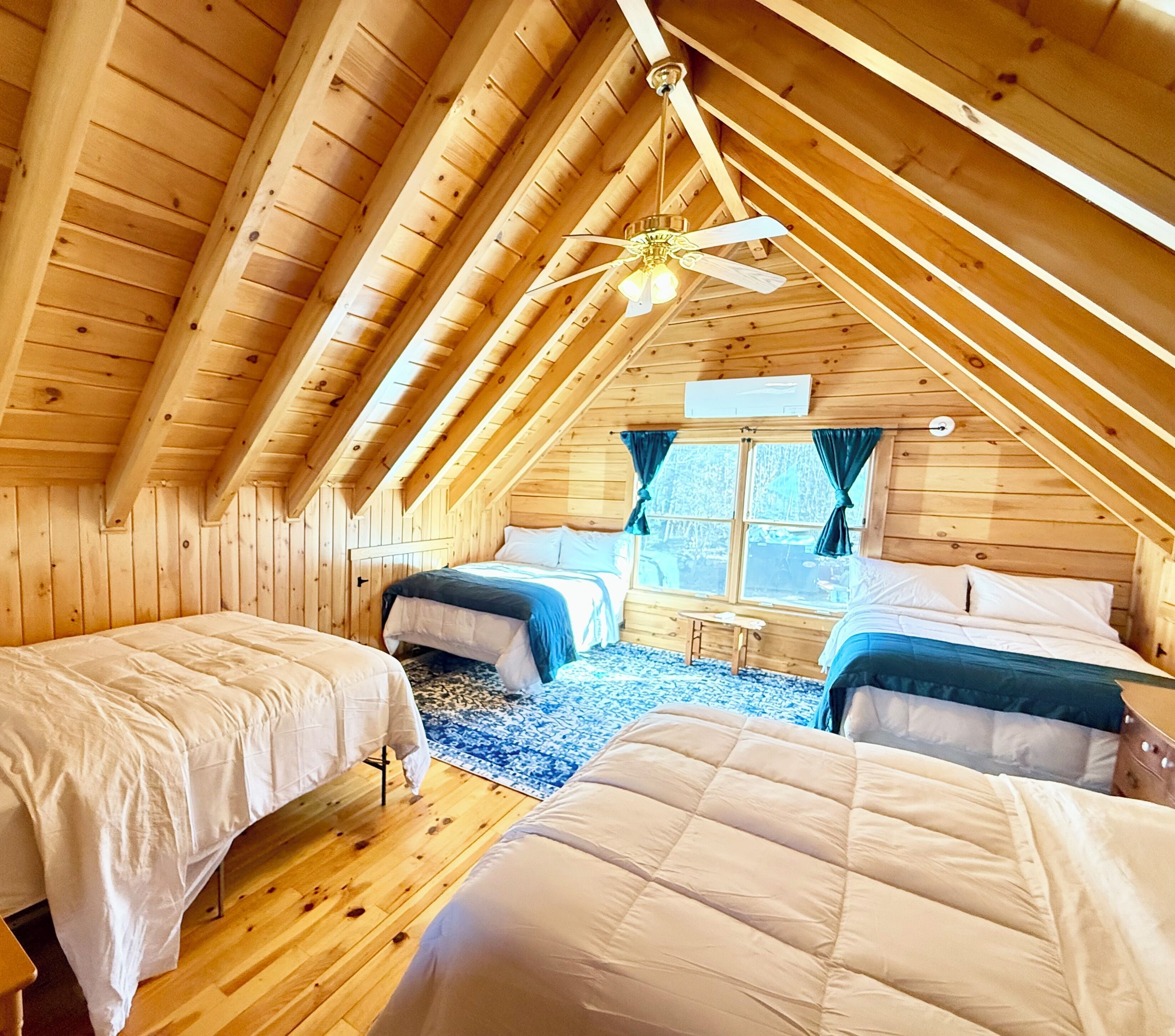 Een zolderkamer met twee bedden, een plafondventilator en een raam met gordijnen.