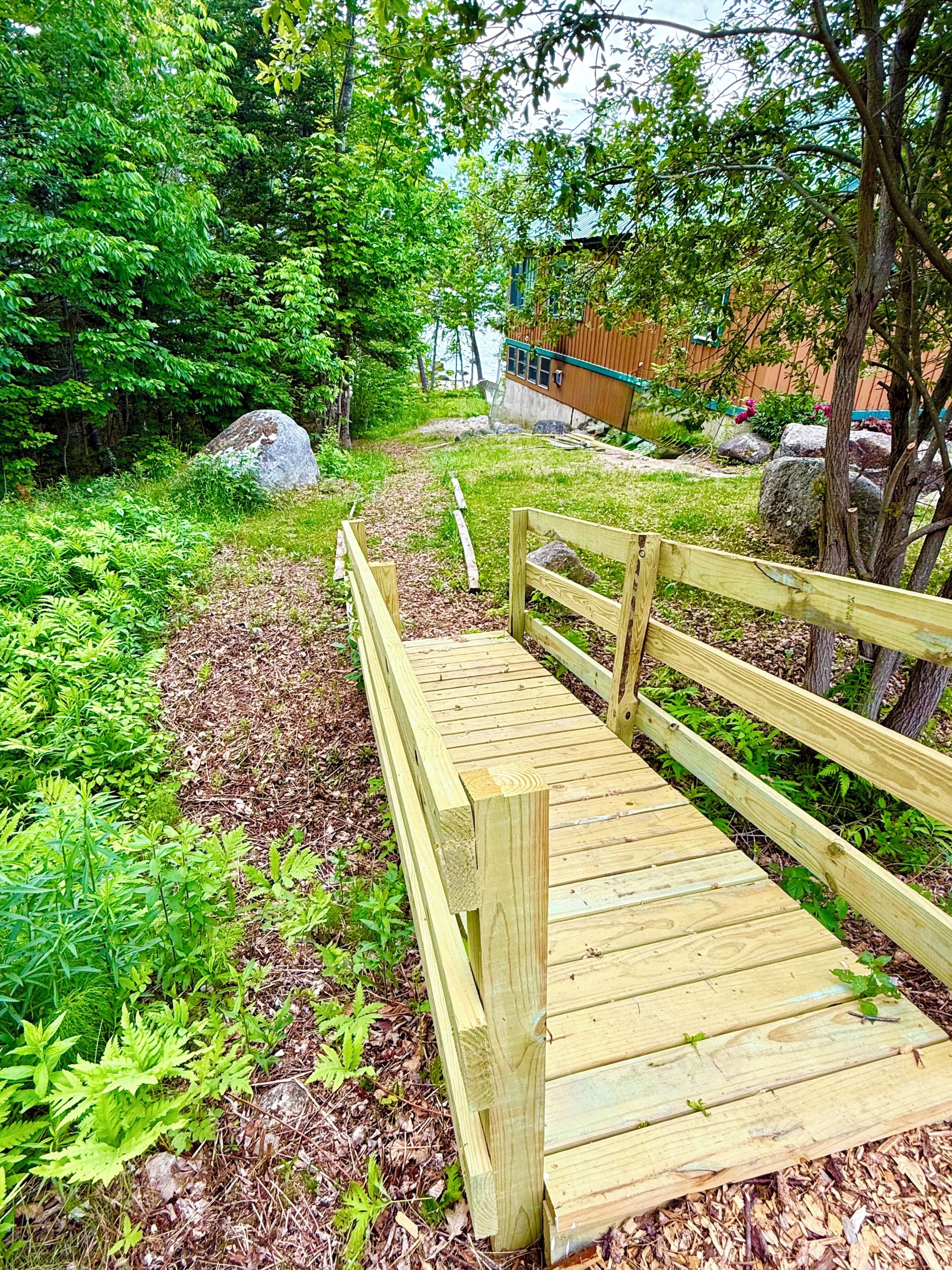 A wooden bridge in a lush, green garden with a house in the background.