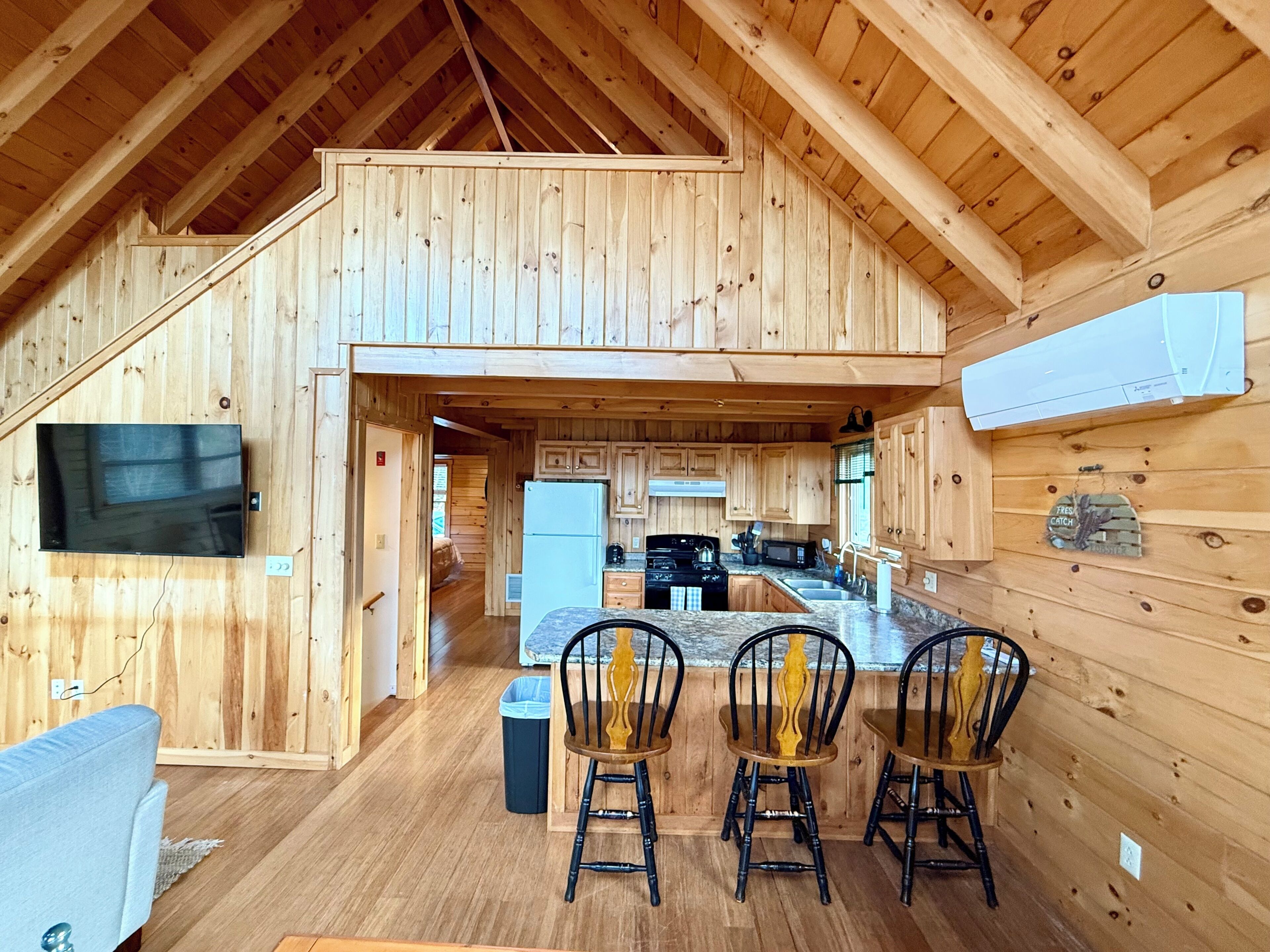 Interior de una cabaña de madera con cocina, comedor y televisor montado en la pared.