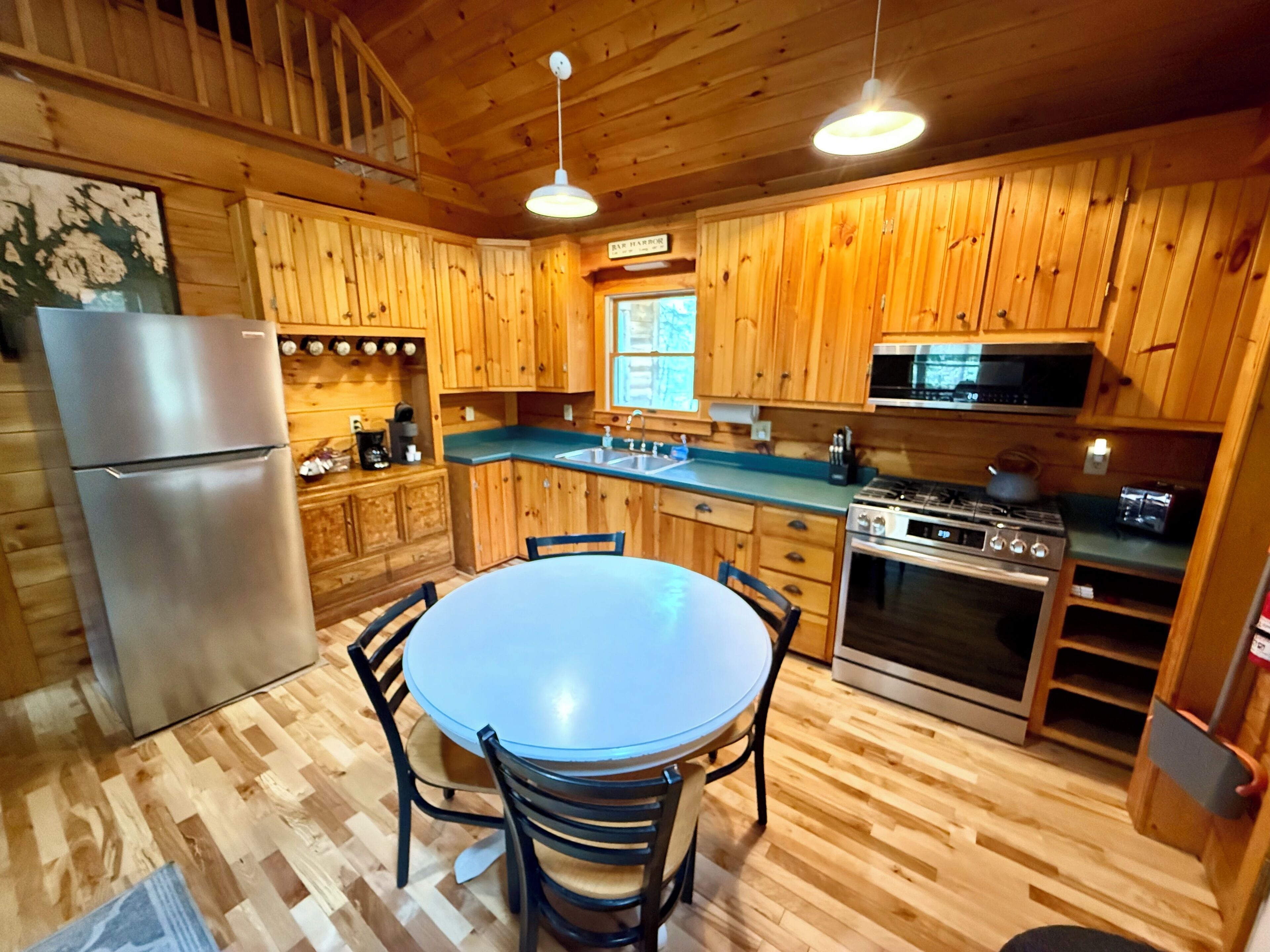 Une cuisine de style rustique, avec des éléments en bois, un îlot central, des appareils en acier inoxydable et un coin repas avec des chaises.
