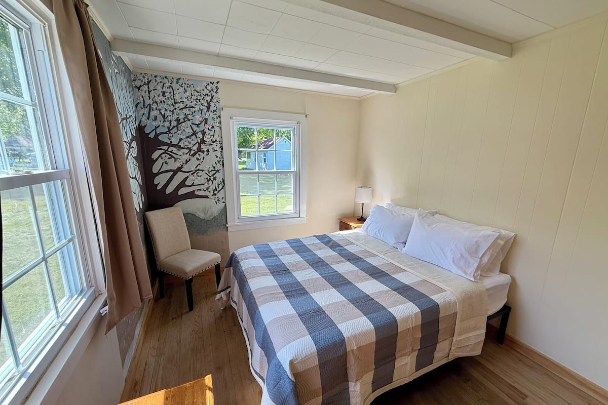 A bedroom with a bed, a chair, a window, and a wall mural.