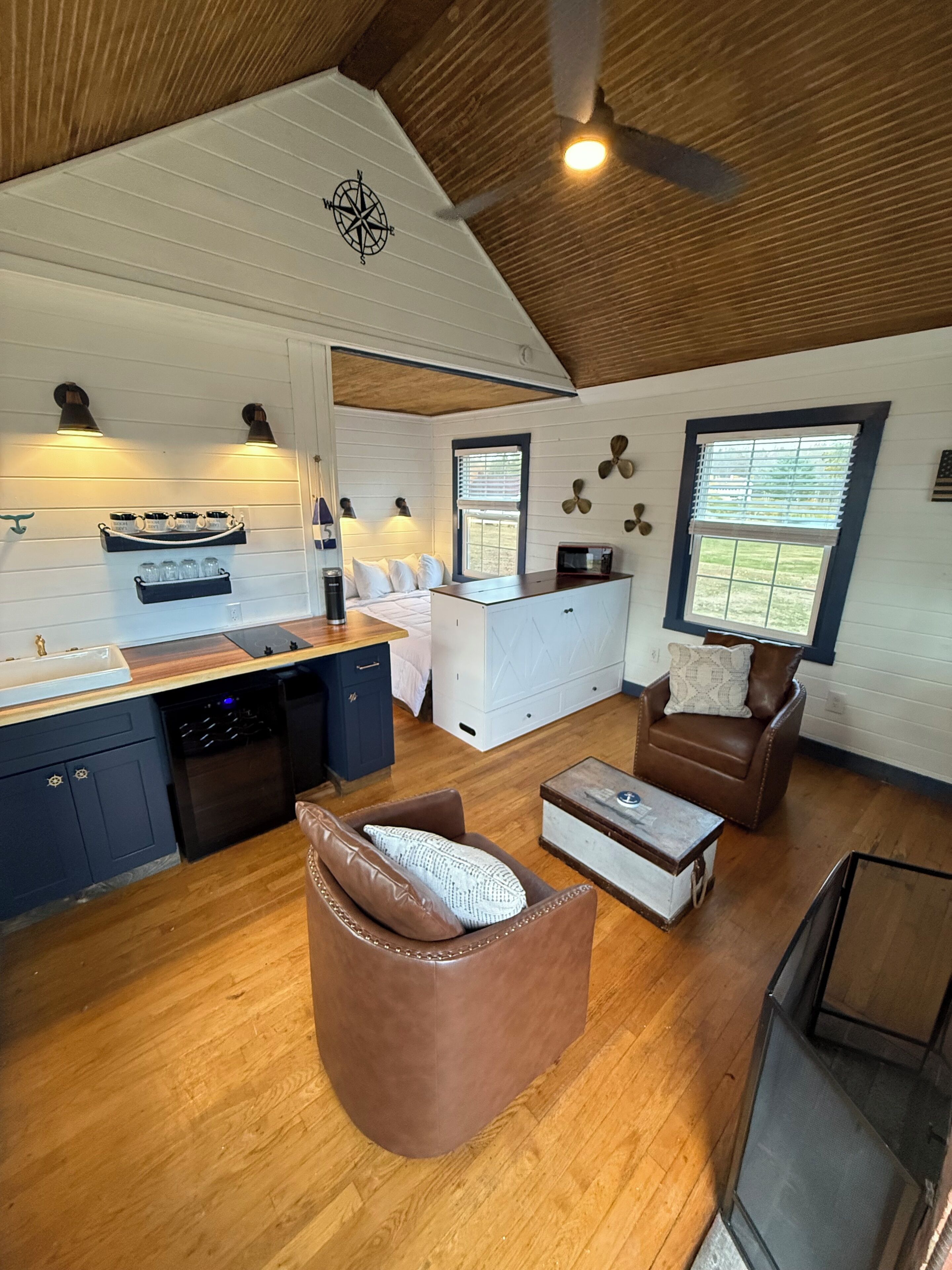 A spacious living area with a kitchen, wooden flooring, and a ceiling fan.