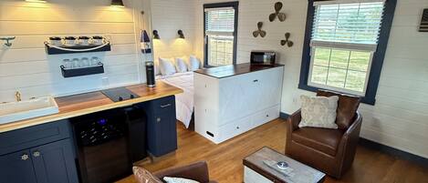 A spacious living area with a kitchen, wooden flooring, and a ceiling fan.