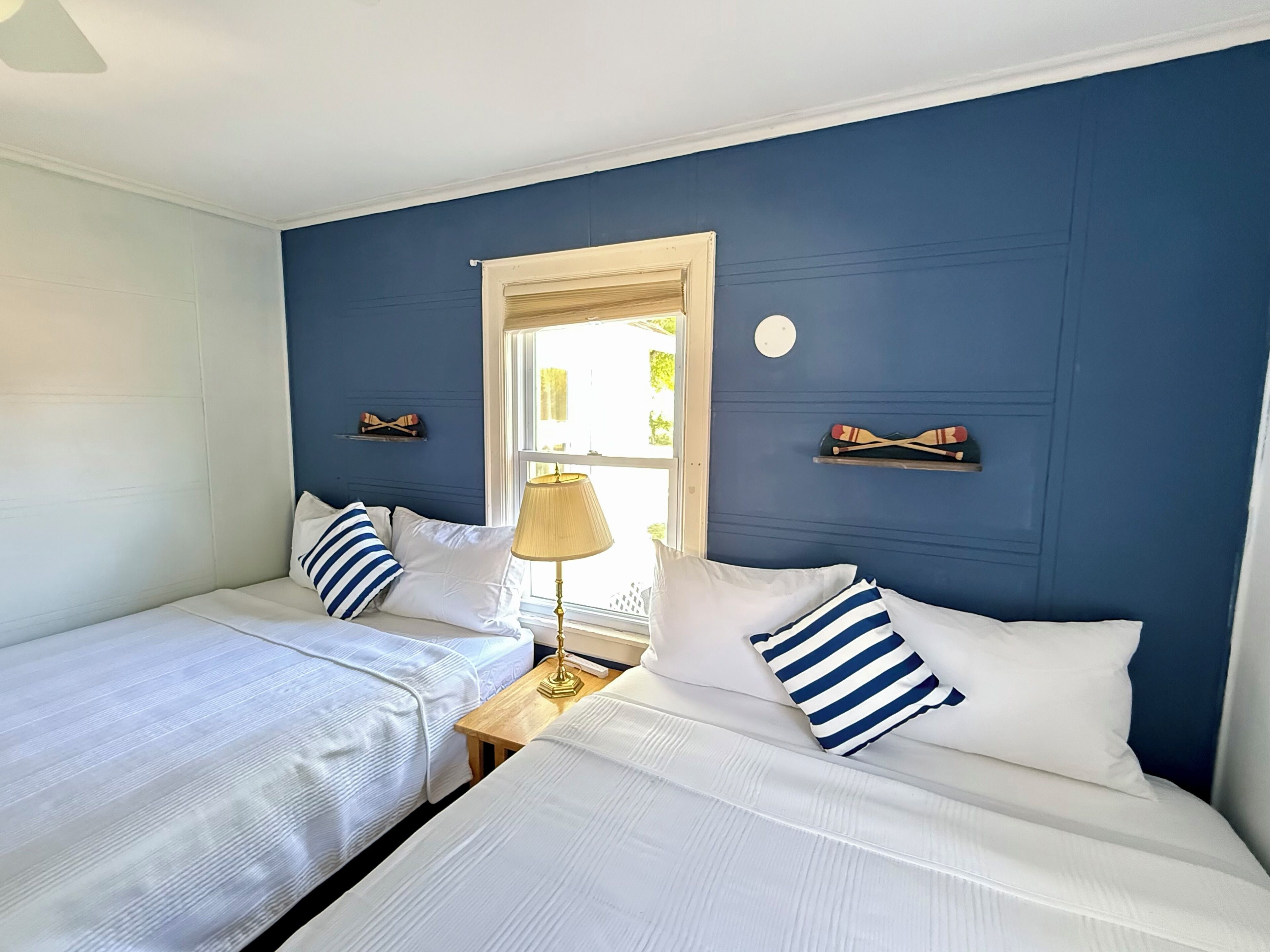 A room with two beds, a window, a lamp, and wall decorations.