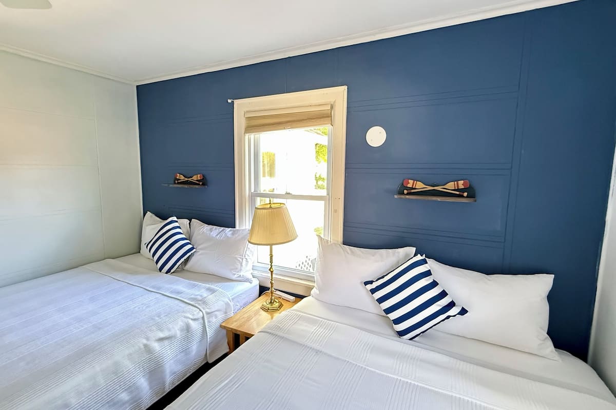 A room with two beds, a window, a lamp, and wall decorations.