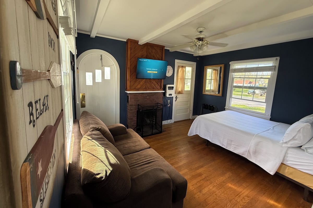 A bedroom with a bed, a wooden floor, a TV mounted on the wall, a fireplace, and a door with windows.