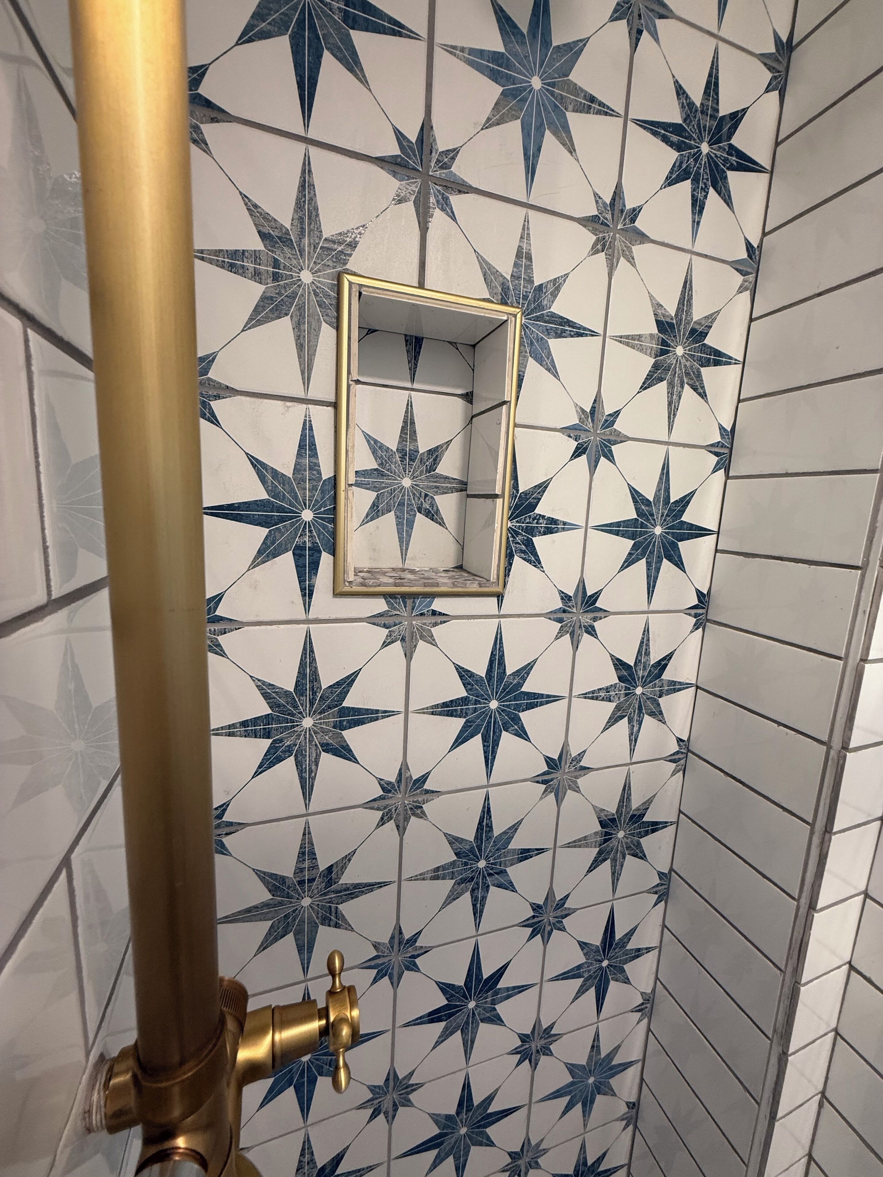 A bathroom with star-patterned tiles, a gold-colored pipe, and a small square mirror.
