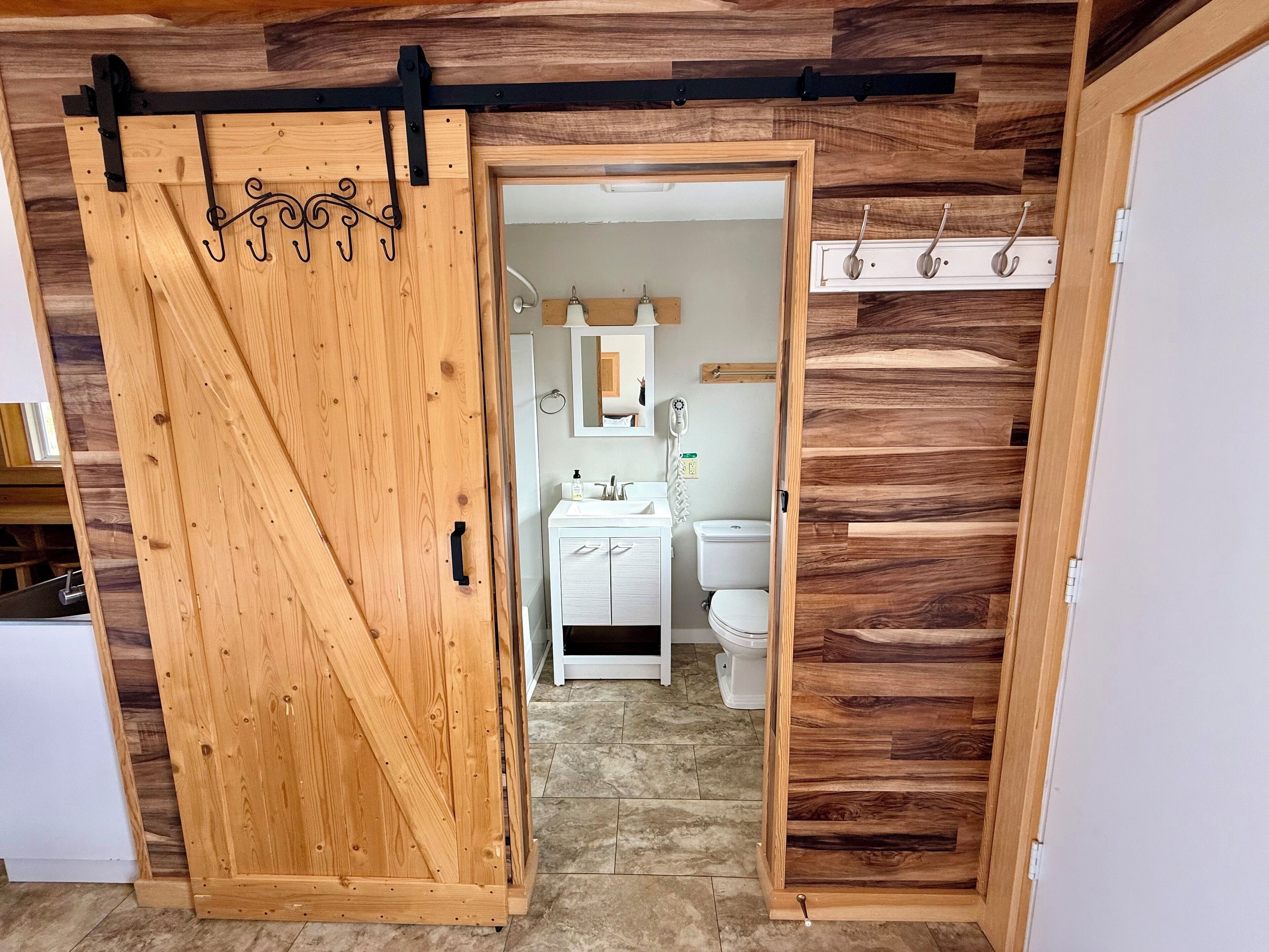 A wooden sliding door leading to a bathroom with a toilet, sink, and mirror.
