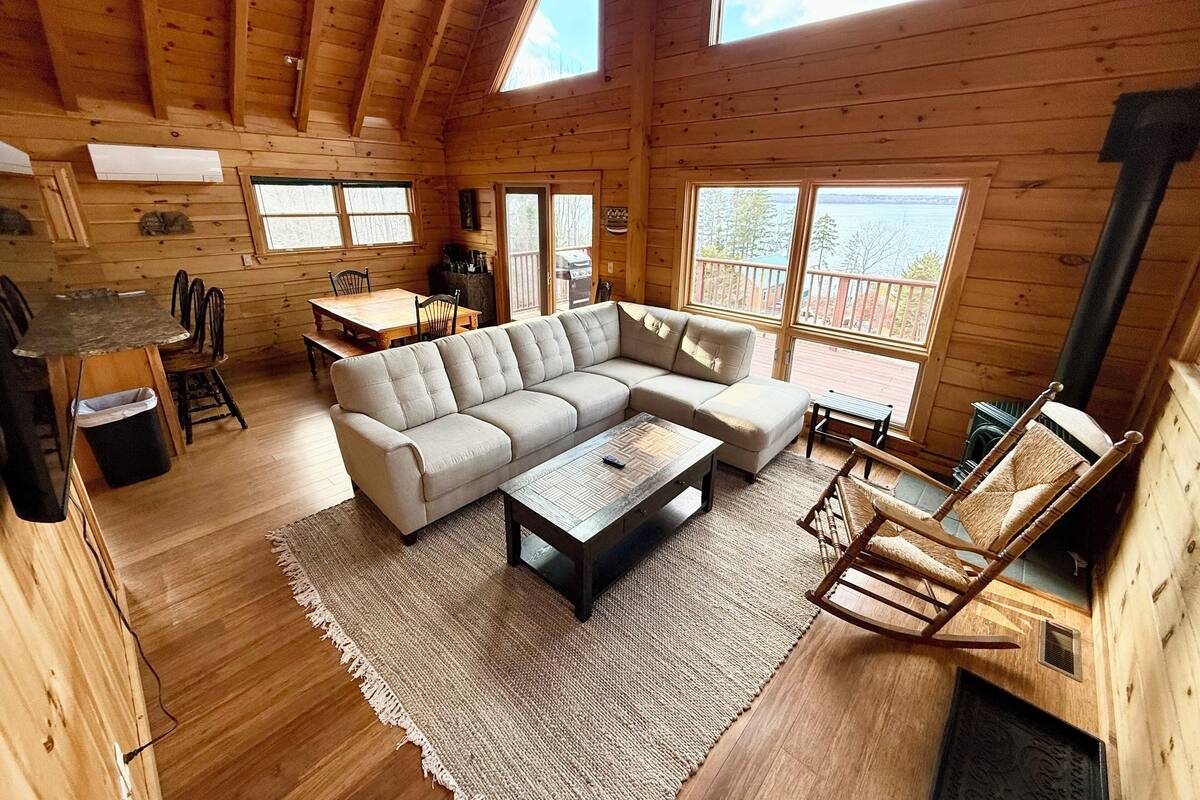 A wooden cabin interior with a sofa, coffee table, dining table, chairs, and a fireplace.