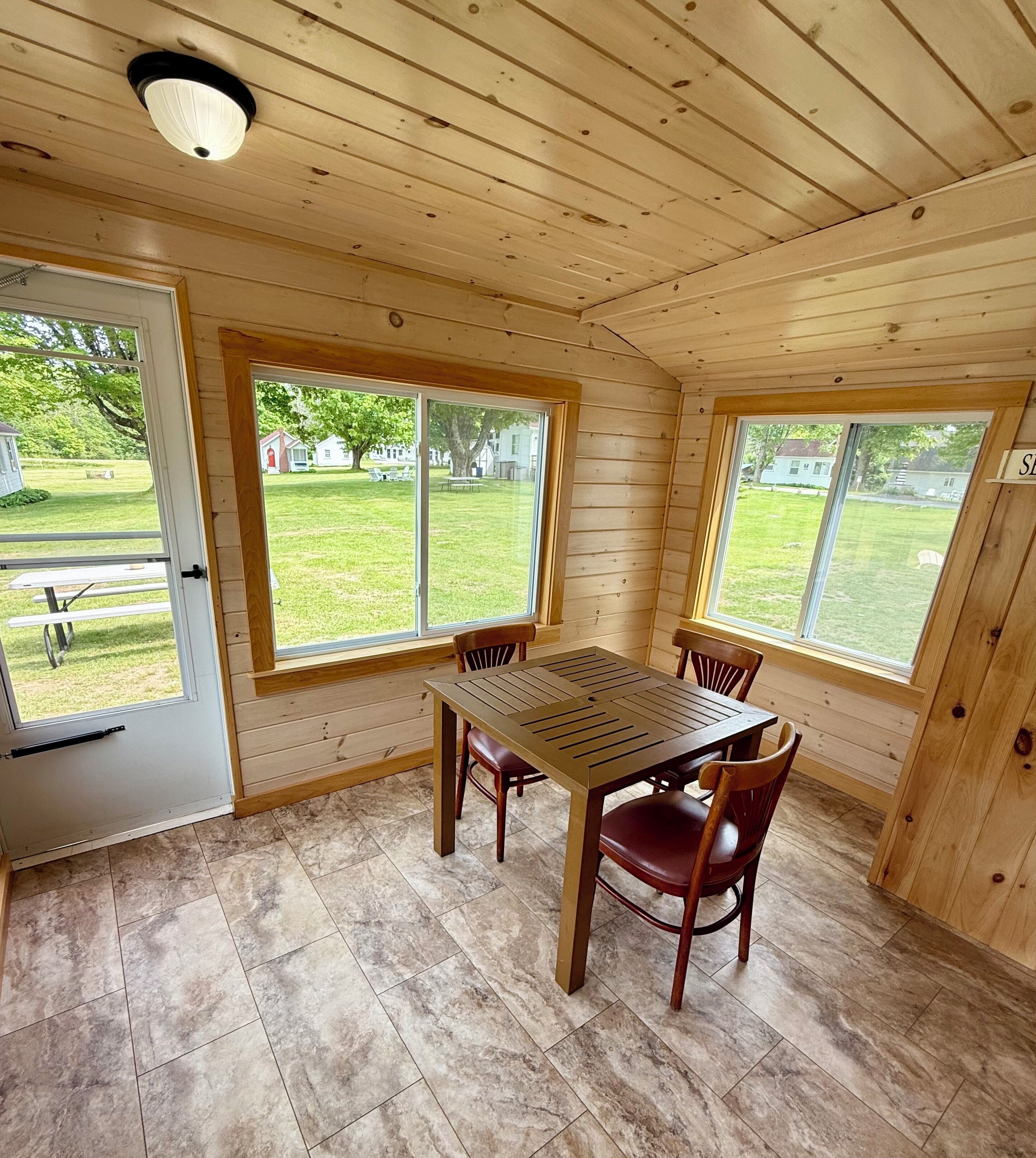 A wooden-paneled room with a table and chairs, large windows, and a door.