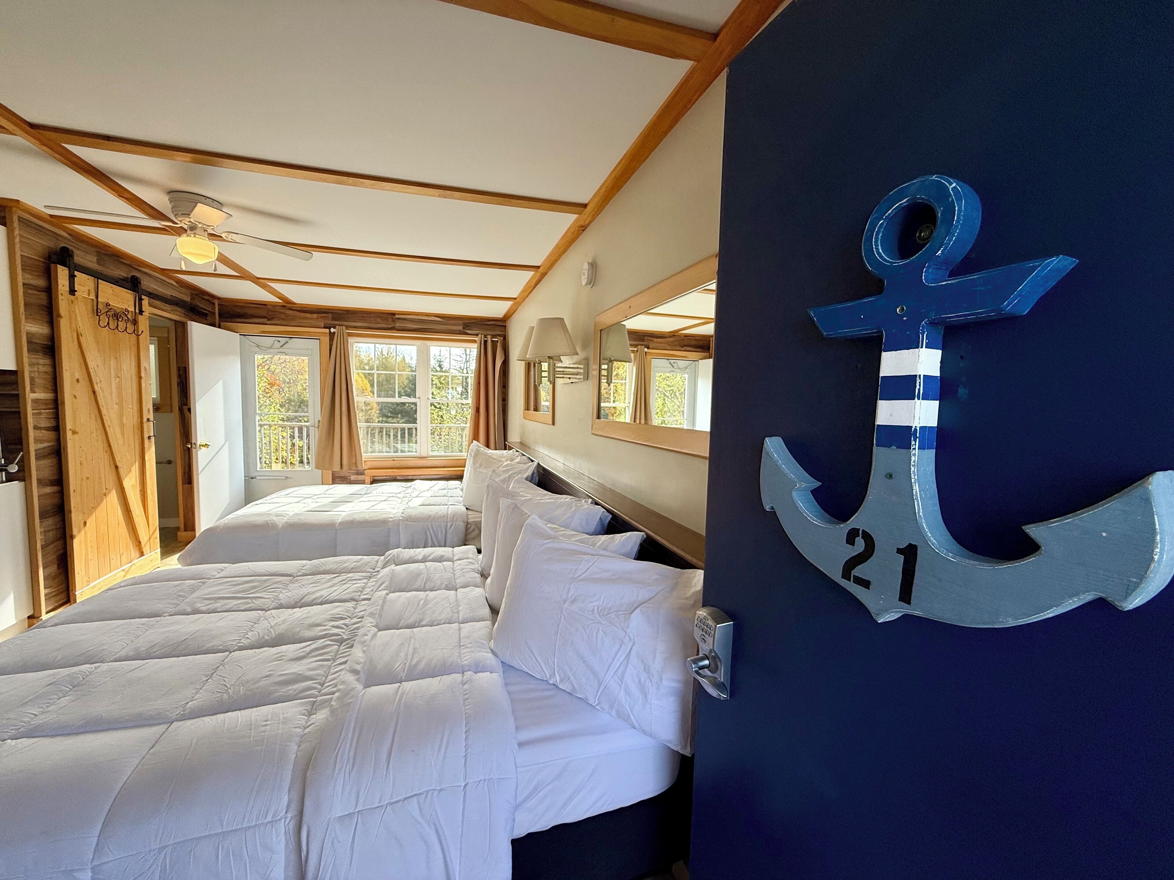 A bedroom with a bed, a wooden door, a window, and a wall-mounted anchor decoration.