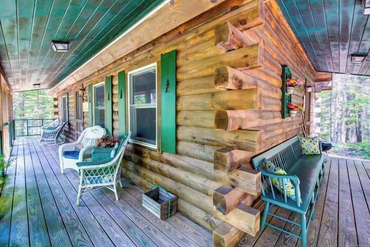 A log cabin with a porch, wooden deck, and outdoor seating area.