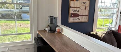Una cocina con encimera de madera, dos taburetes, una cafetera y un letrero en la pared con texto.