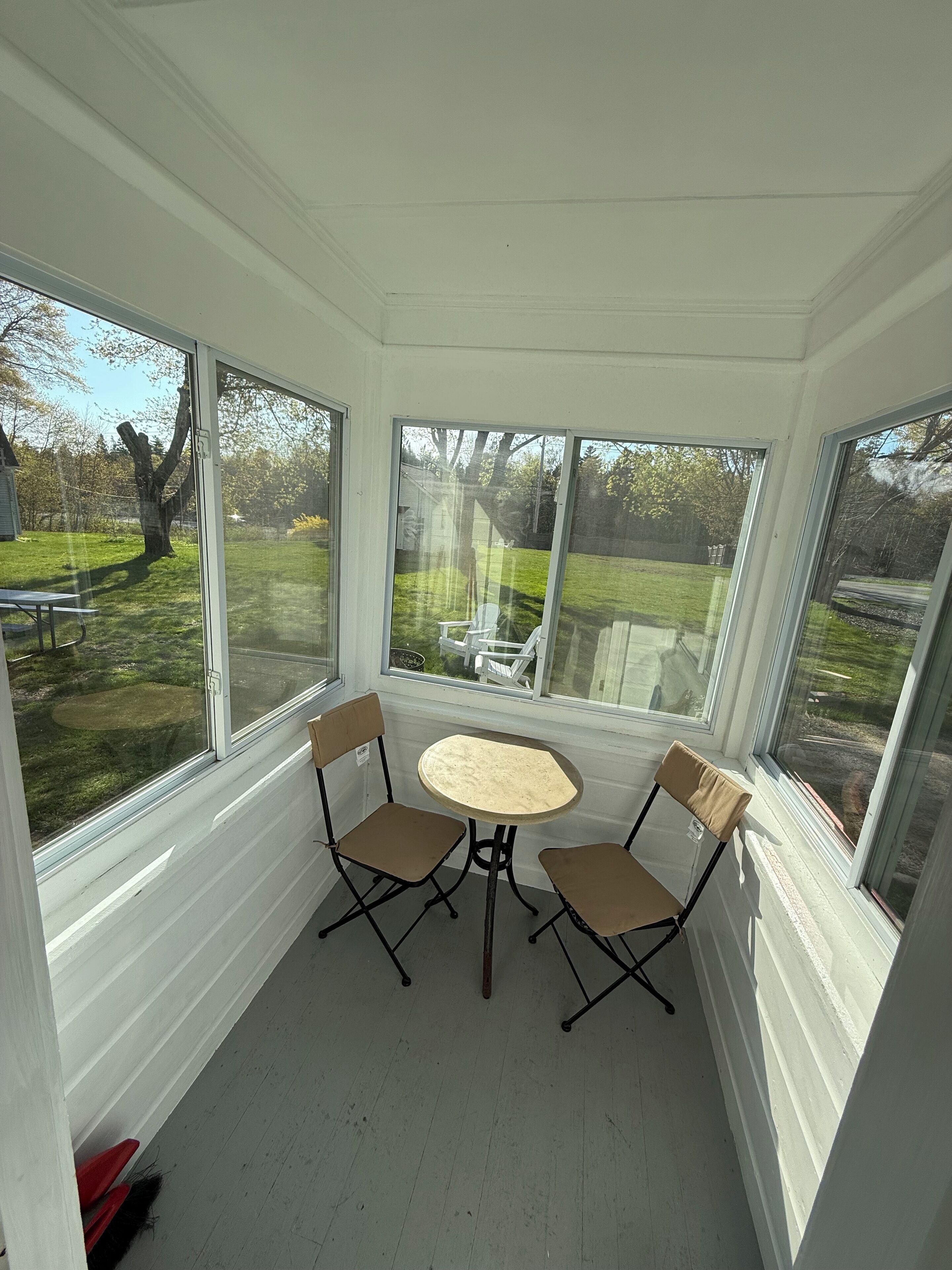 Een zonnedek met een tafel, twee stoelen, grote ramen en uitzicht op een tuin.