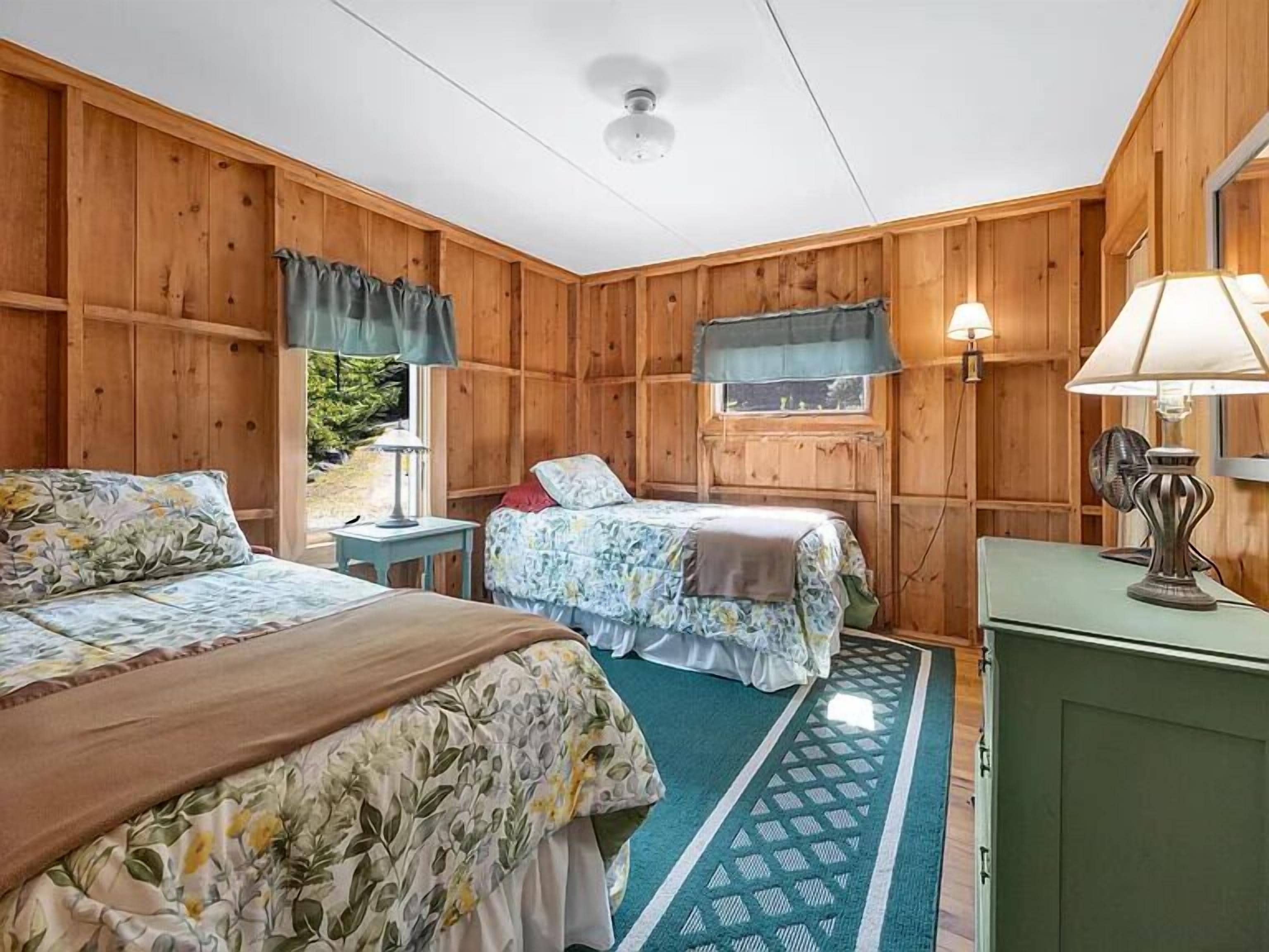 A room with two beds, a window with curtains, a lamp, and a fan.