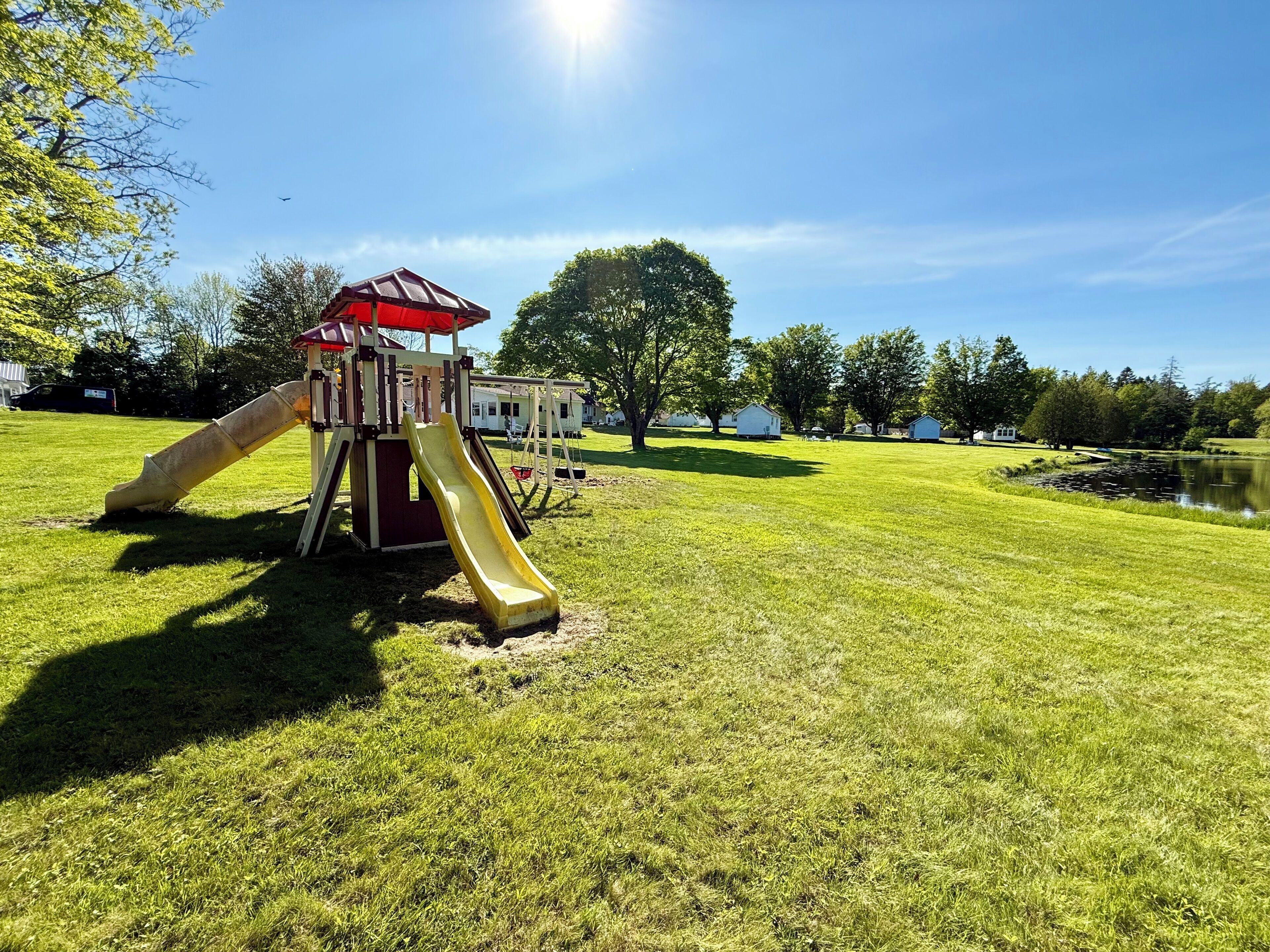 A playground with a slide and swing set, surrounded by a grassy field and trees.