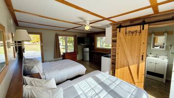 Ein Schlafzimmer mit zwei Betten, einem Deckenventilator, einem Holzschrank, einem Badezimmer mit Spiegel und Waschbecken sowie Blick ins Freie.