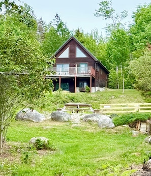 A wooden cabin with a balcony, surrounded by lush greenery and rocks. - Eden Village Motel & Cottages (Bar Harbor)