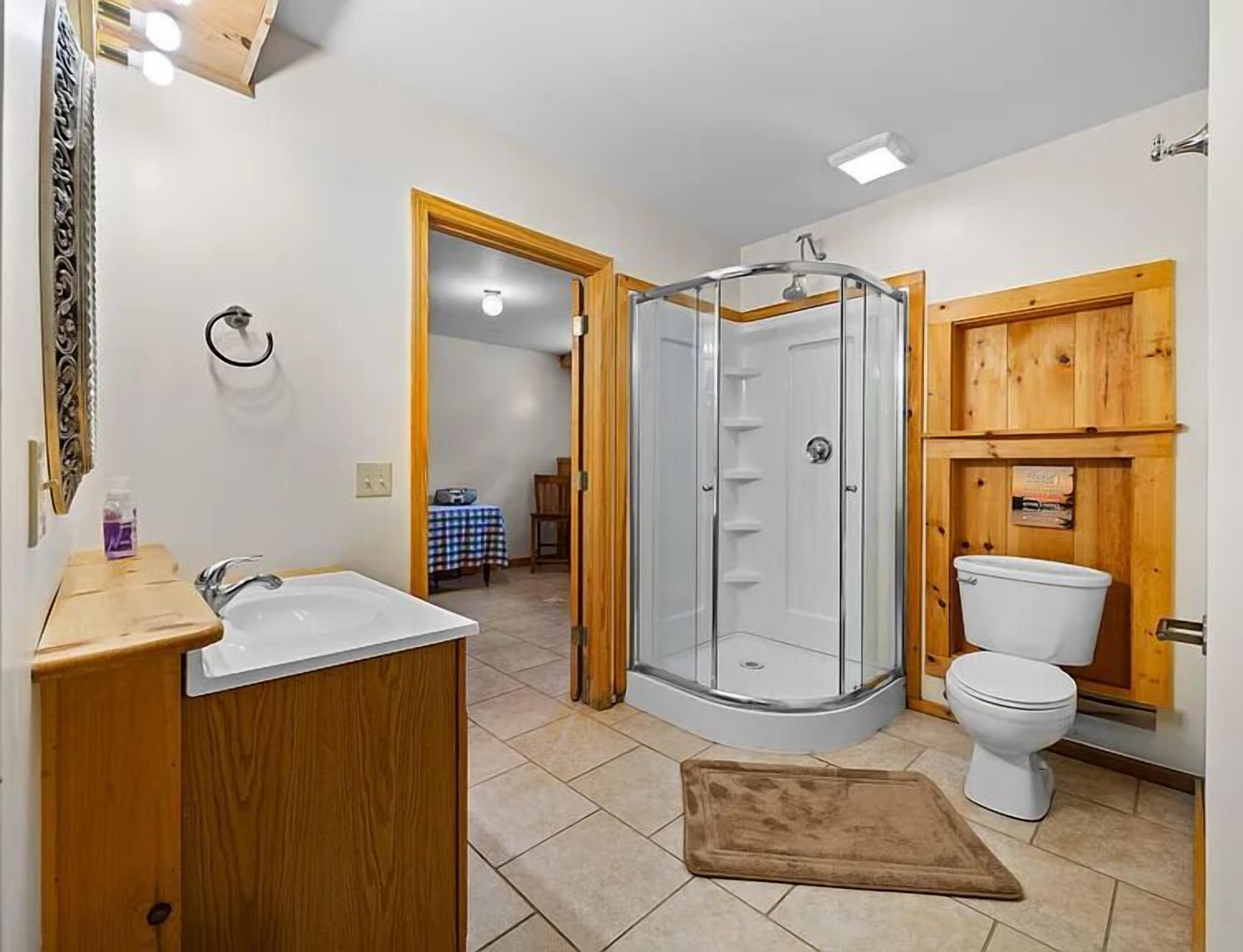A bathroom with a shower, toilet, sink, and a wooden vanity.