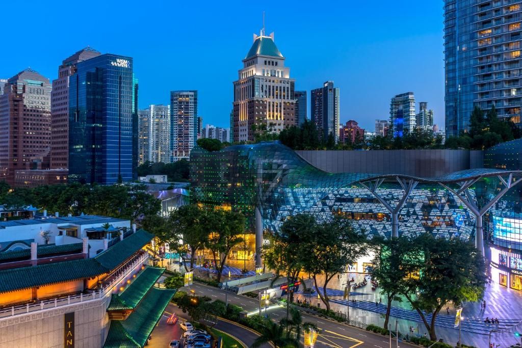 A modern cityscape with high-rise buildings, a distinctive glass structure, and a traditional building with a green roof.