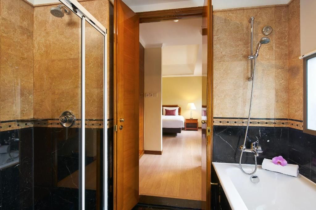 Un baño de hotel con ducha, lavabo y una puerta que da a un dormitorio.